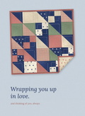 Wrapping you up in love. Sympathy card with a stitched patchwork quilt in navy, rose, sage and oat, one corner folded back, on dusty blue